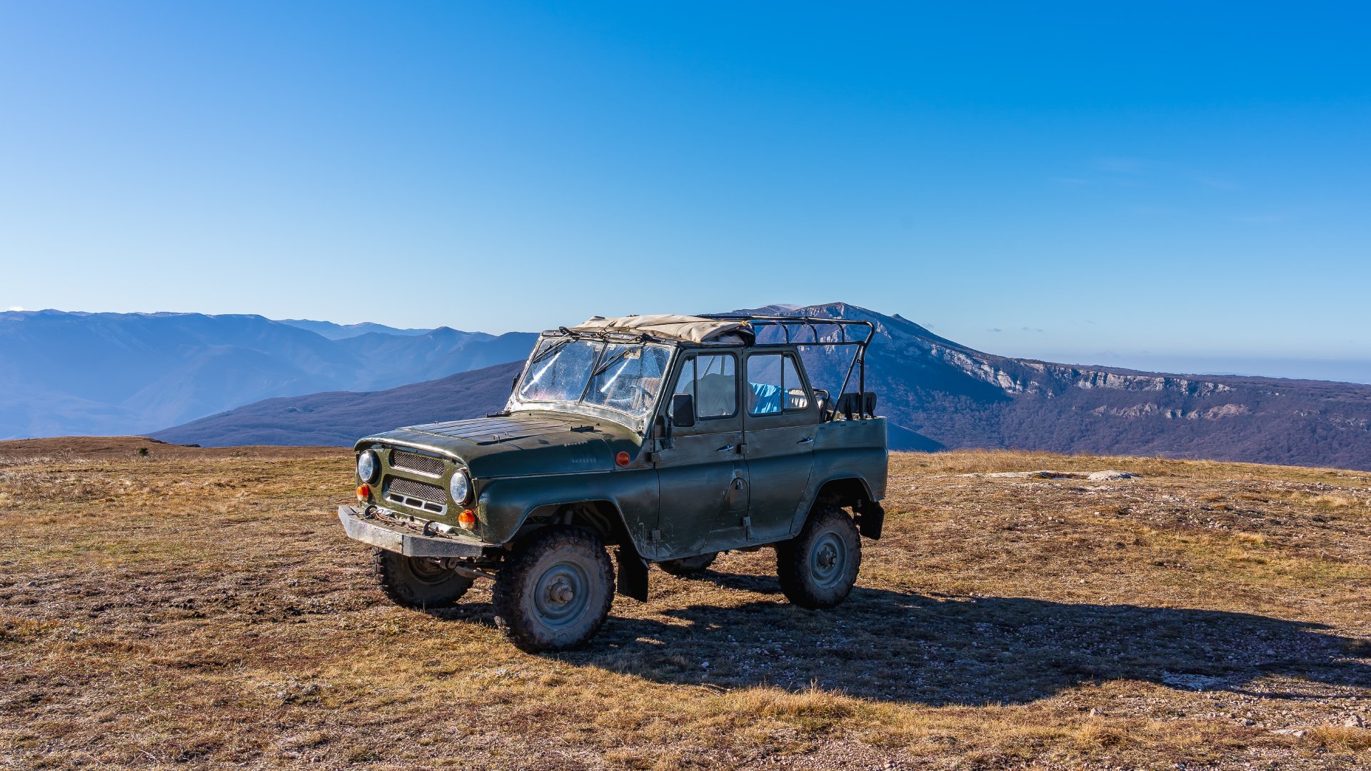 An old vintage Jeep finished in a classic forest green color parked in a grassy field atop a mountain.