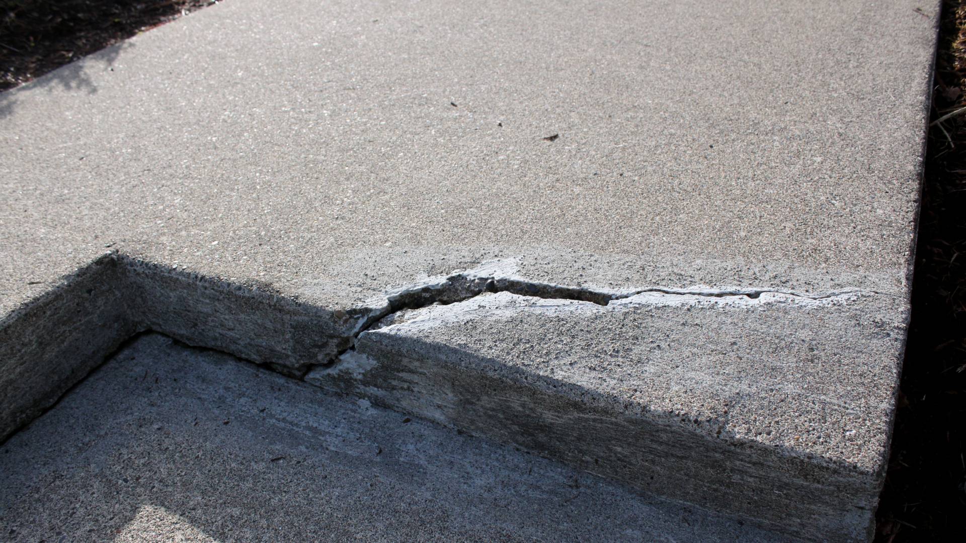 A close-up of a damaged concrete step with a deep crack starting at the base and moving up and over to one side of the step.
