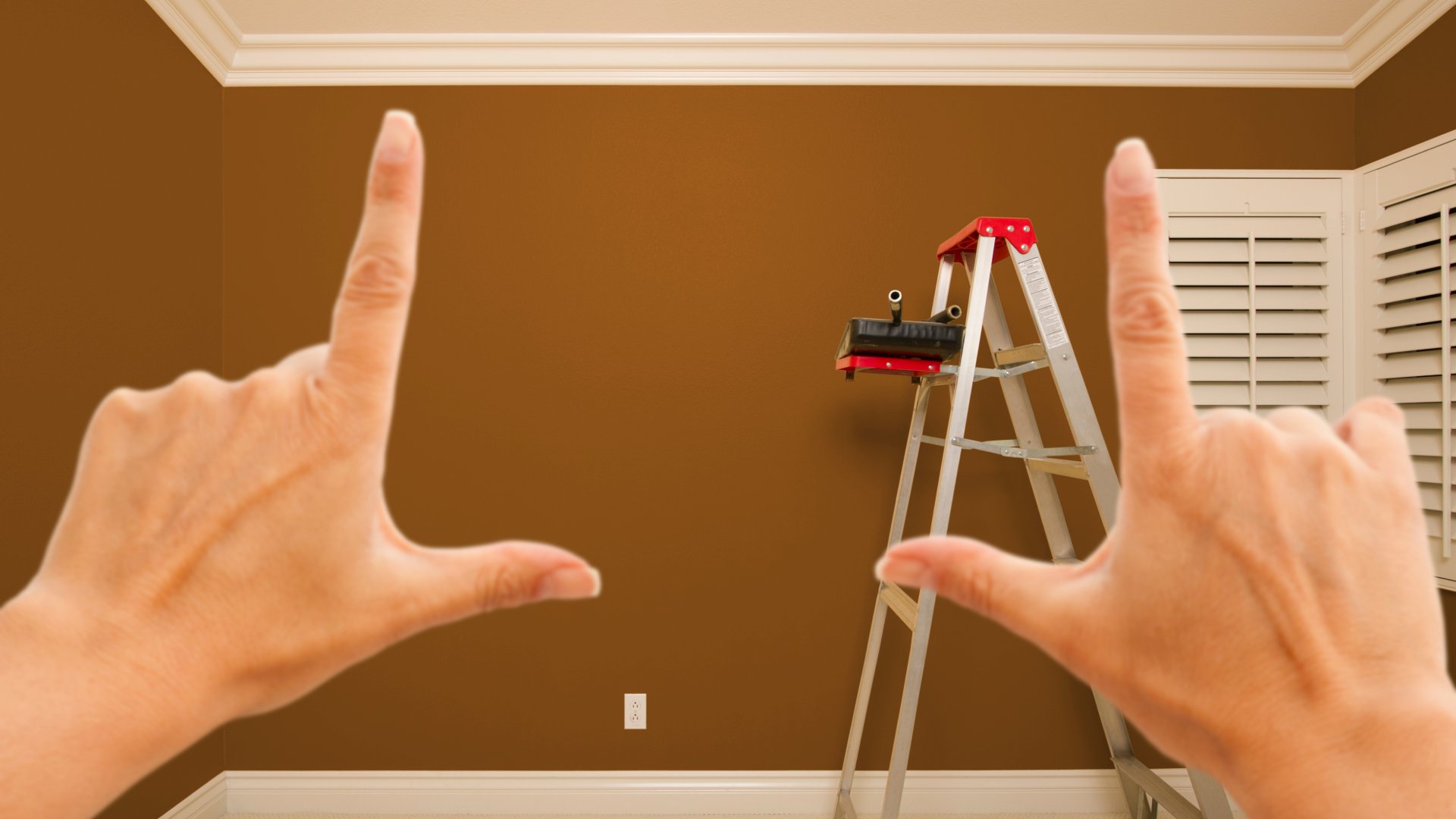 A closeup of two hands framing in the view of a room inside of a home to envision a construction project.