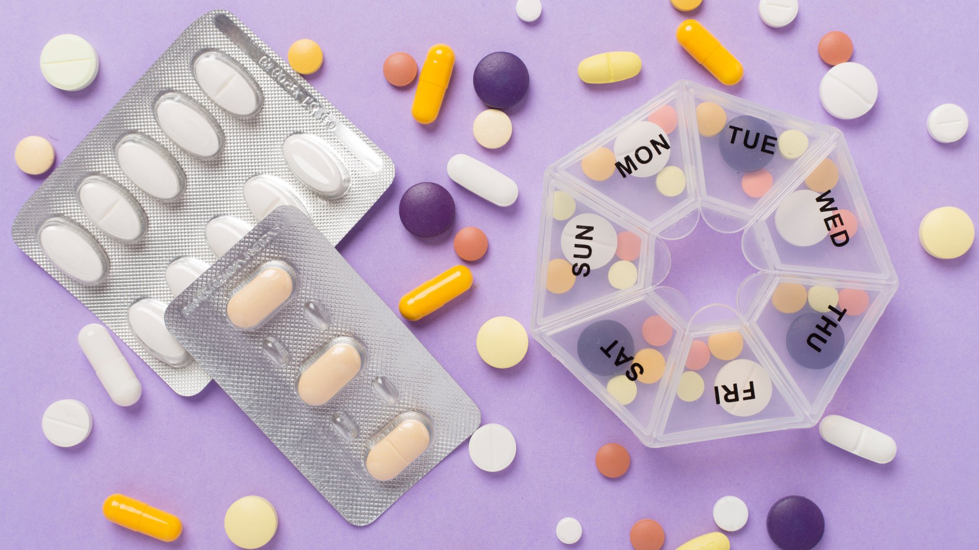 A daily pill organizer filled with a variety of colorful pills. There are pills in two foil packets next to the organizer.