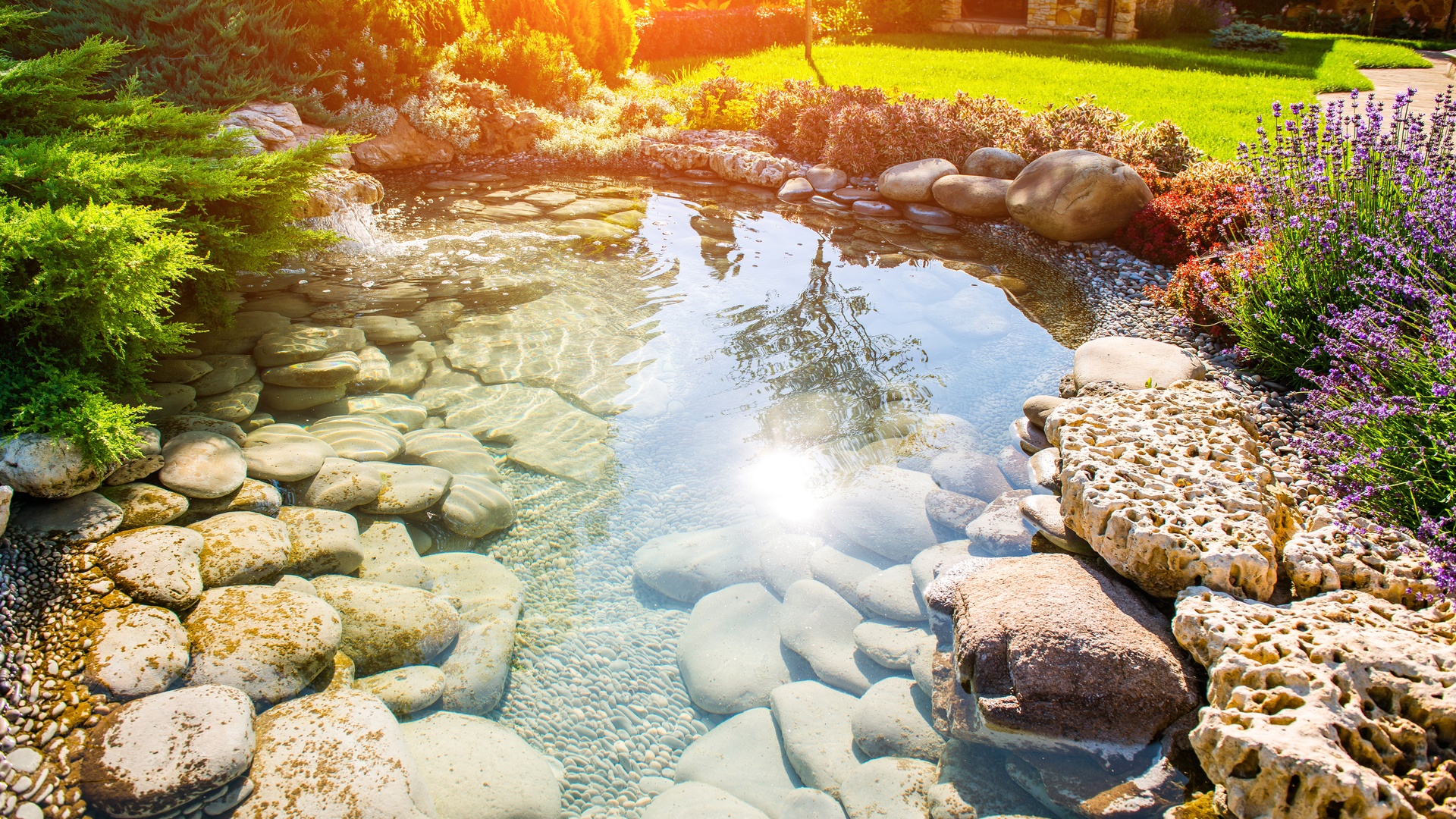 A beautifully manicured residential landscape with a water feature on the property. The pond is full of rocks.