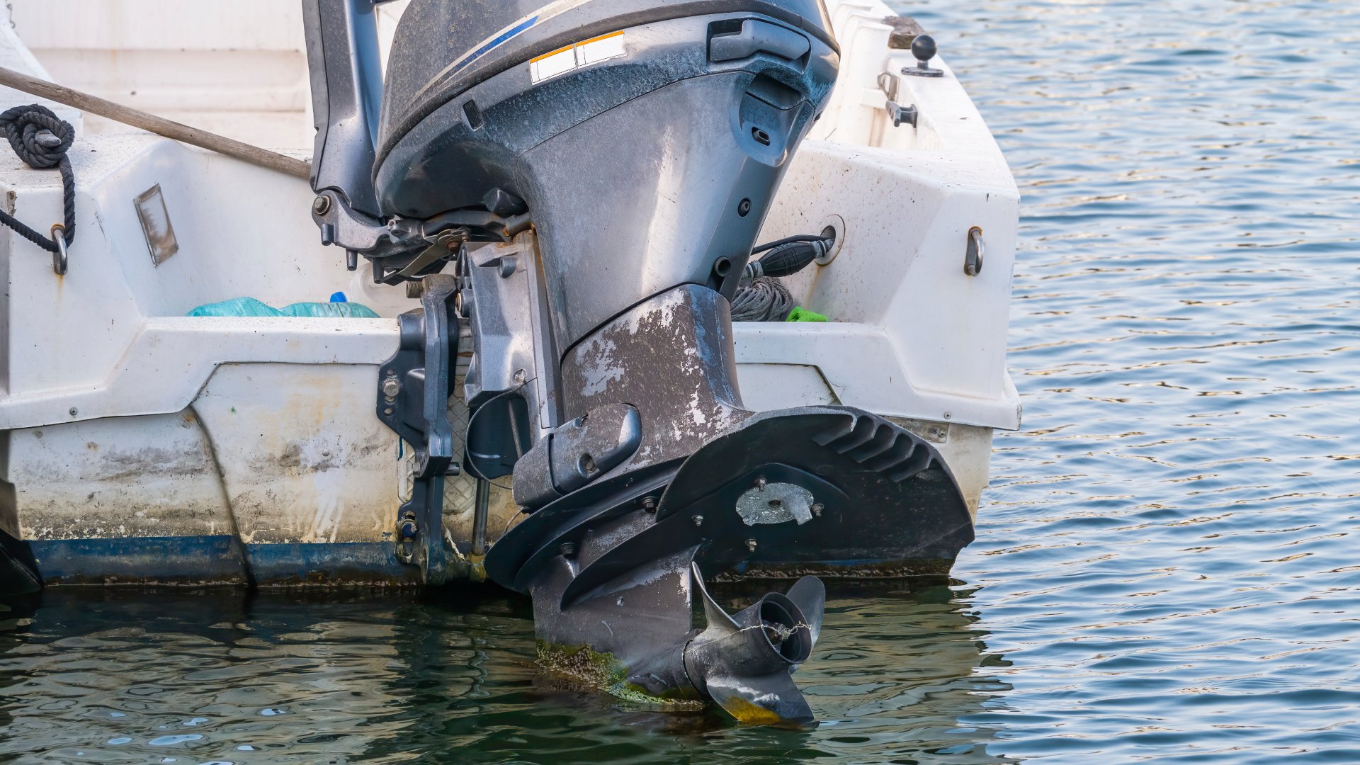 A close-up of a rusted and worn-out engine equipped to the back of a white boat that's out on the water.