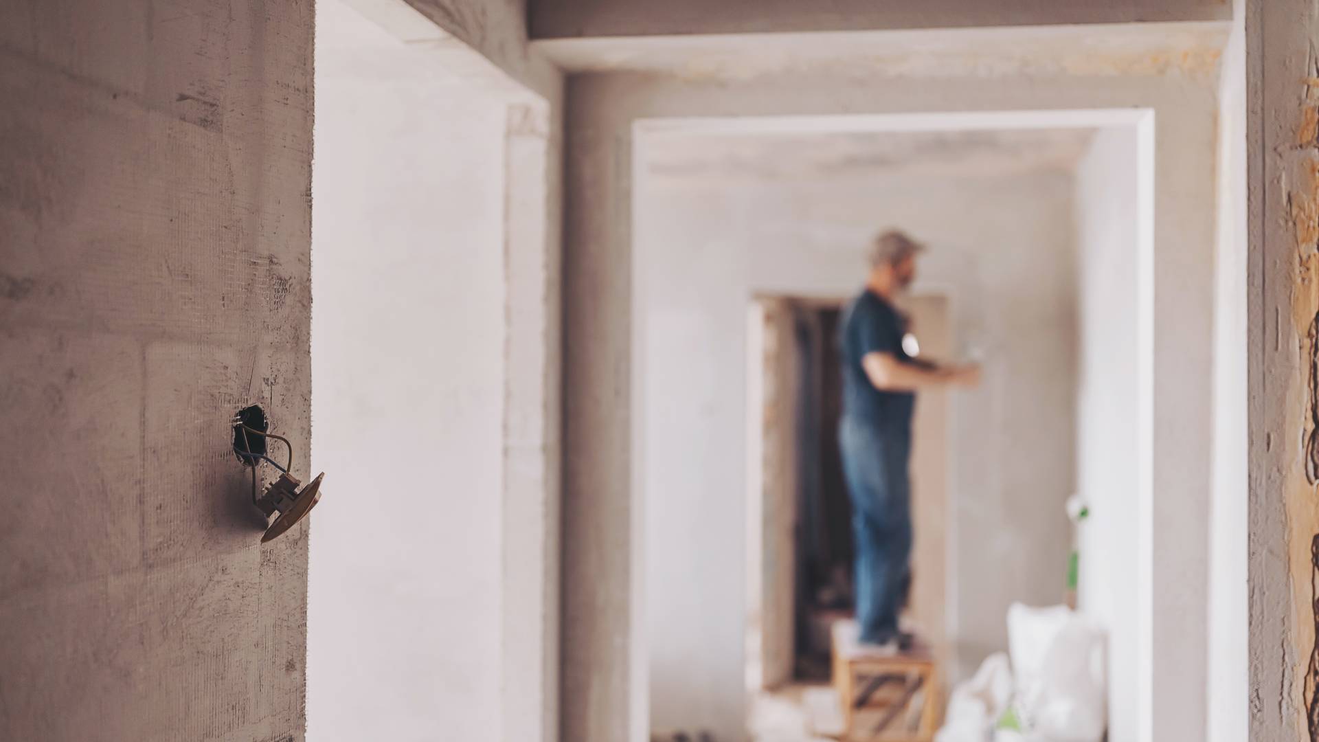 A wall in a building is under construction, with visible scaffolding and a worker wearing a hard hat in the background.