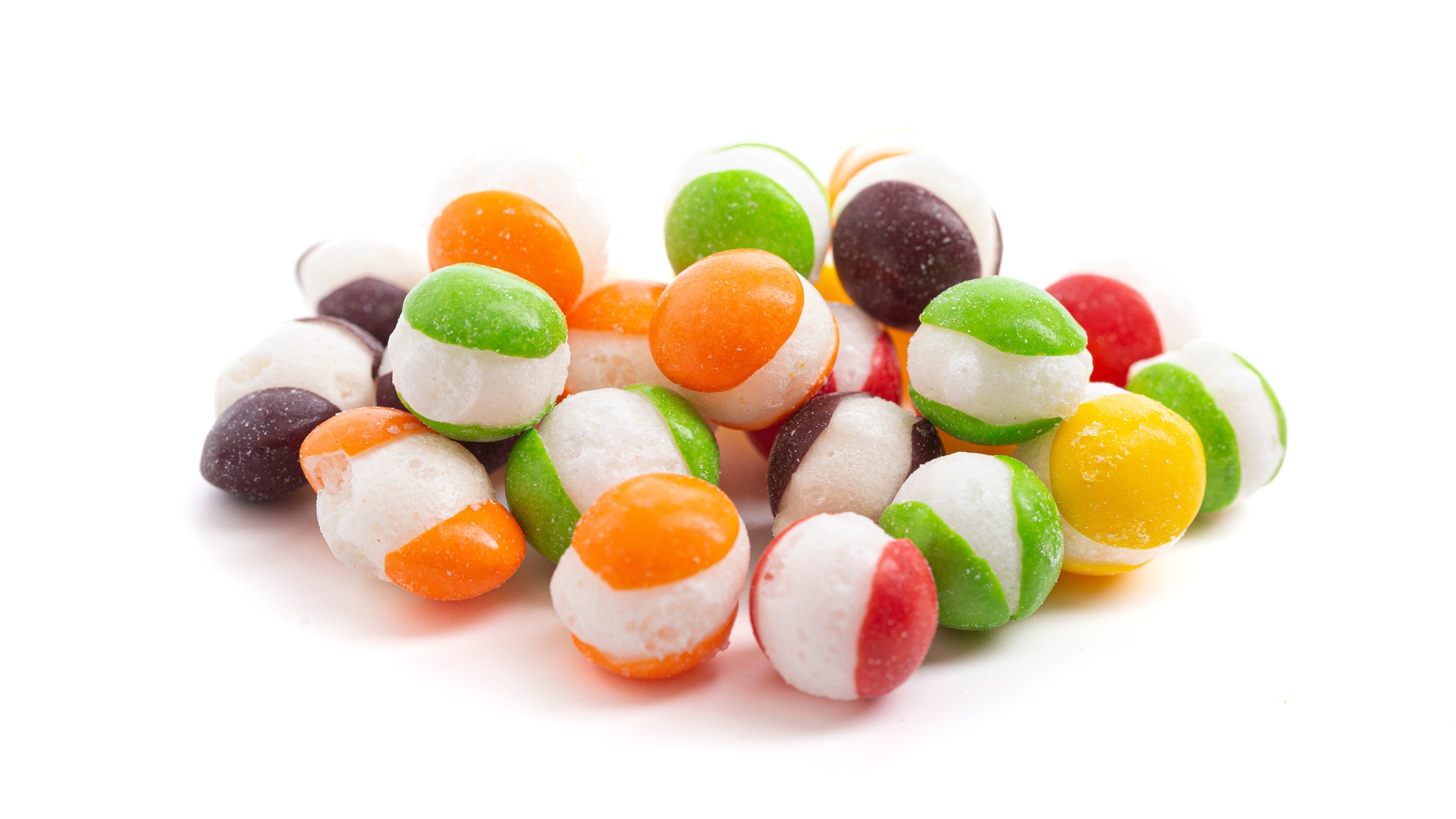 A close-up of freeze-dried rainbow candy on a white table. The candy has colorful tops and bottoms with a white center.