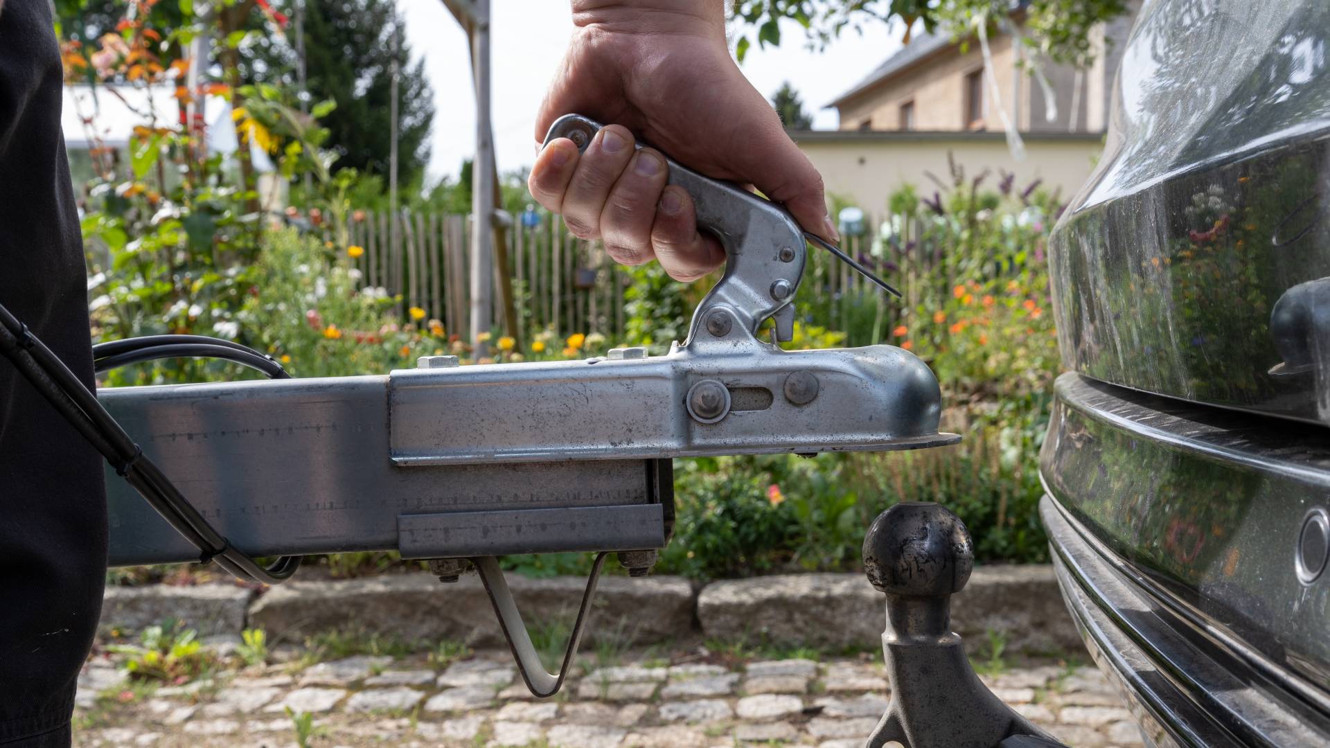 A close-up of a hand attaching a trailer to a vehicle by putting the trailer hitch lock over the towing ball.