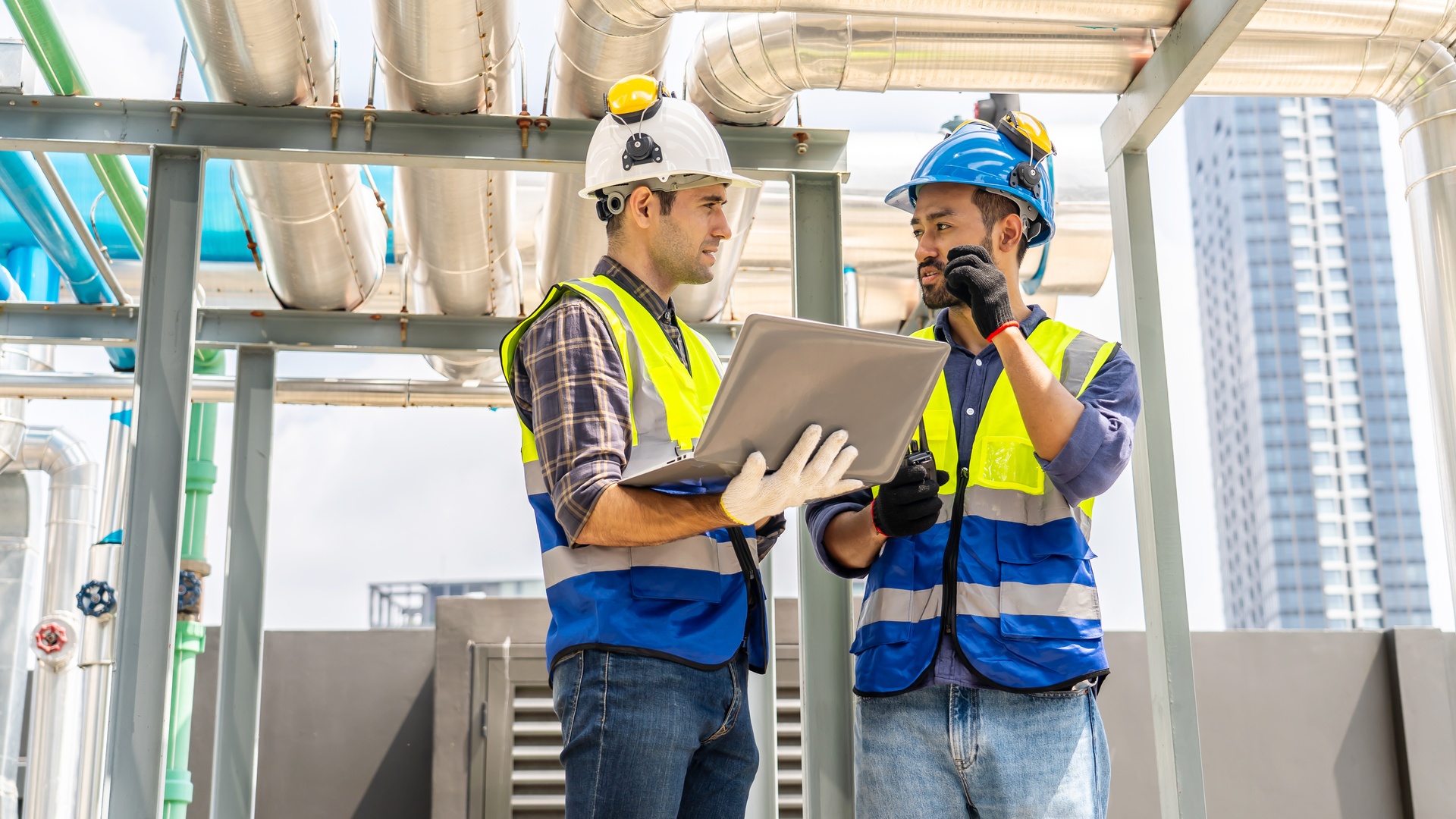 A pair of construction workers wearing hard hats and bright safety vests speak together while on a jobsite.