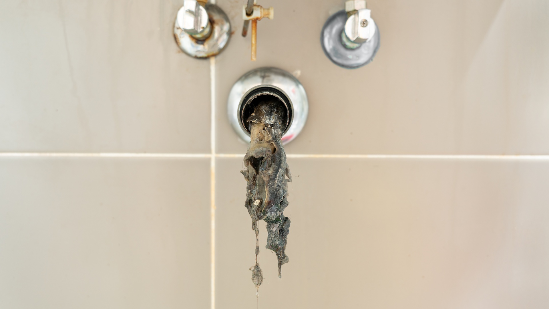 An open pipe extending from a wall with an unknown slimy substance spilling out and dangling from within.