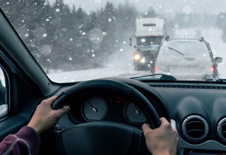 The point of view of a man driving in winter on a snowy road. Snow is falling and traffic is in front and coming toward him.