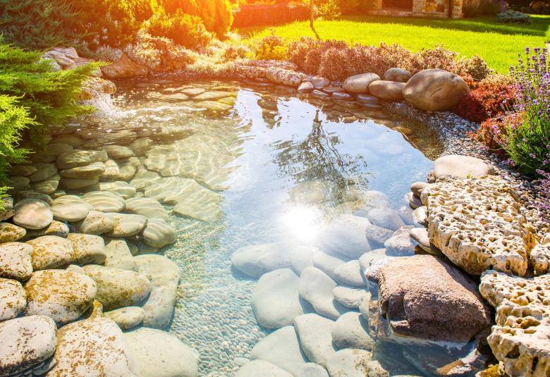 A beautifully manicured residential landscape with a water feature on the property. The pond is full of rocks.