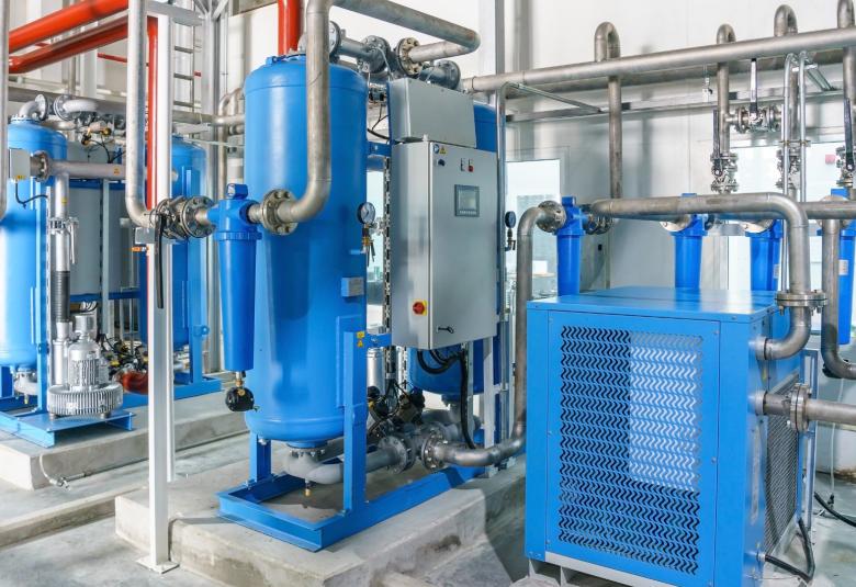 A blue refrigerated air dryer for compressor air on a concrete floor in a bare room with white walls.