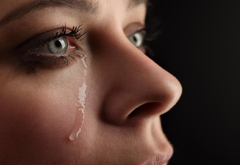 An extreme close-up shows a woman's green eyes and a single tear dripping down her cheek. She is wearing mascara.