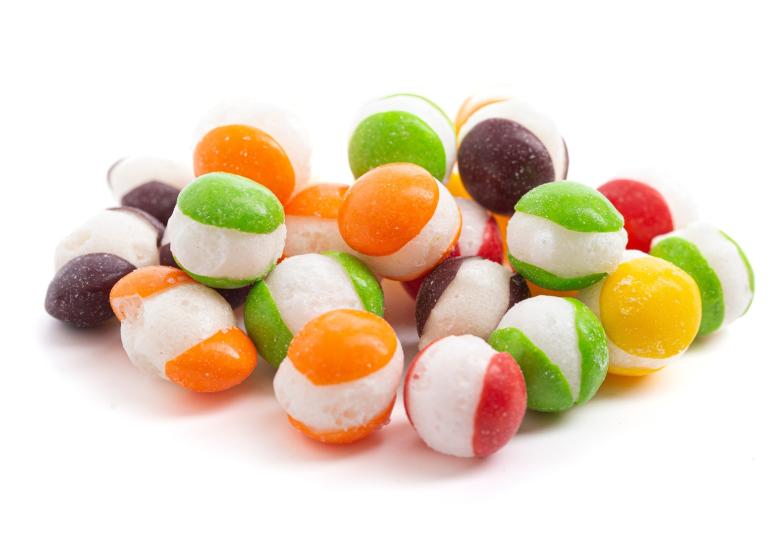 A close-up of freeze-dried rainbow candy on a white table. The candy has colorful tops and bottoms with a white center.