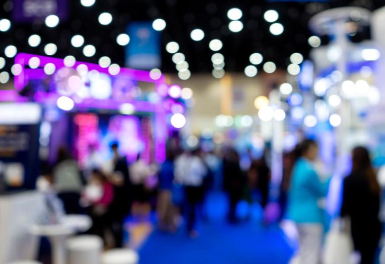 a blurred image of a trade show convention with twinkling lights and a large crowd of people walking around.