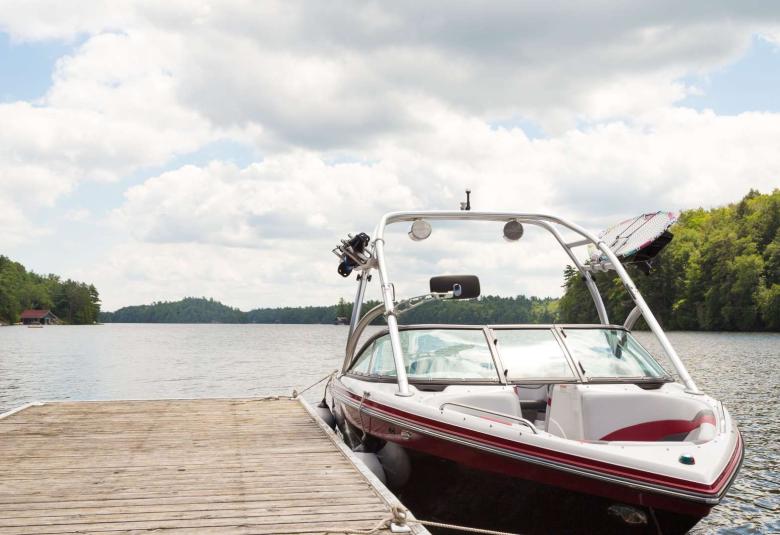 A black, red, and white boat sits in a large body of water. The boat is tied up to a large, tan dock.