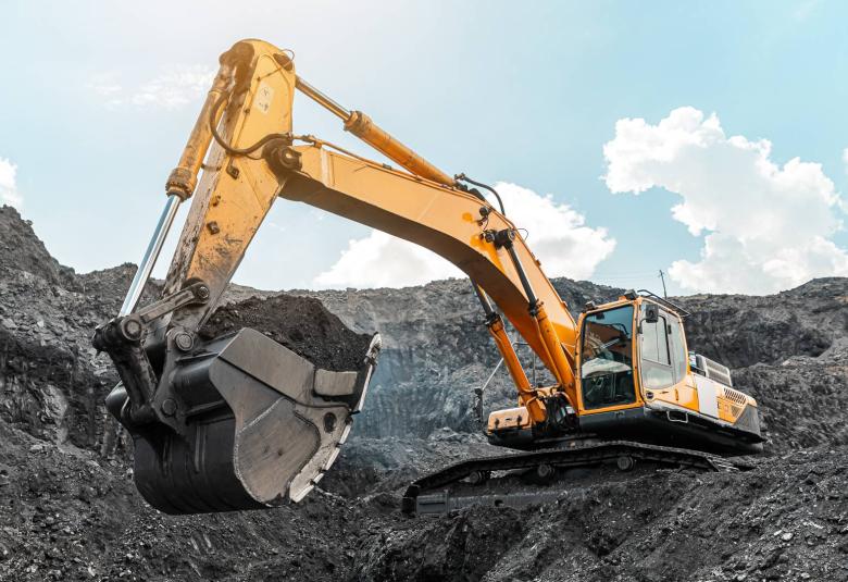 A large excavator sits on top of a hill in a mining quarry, shoveling large amounts of mined material.