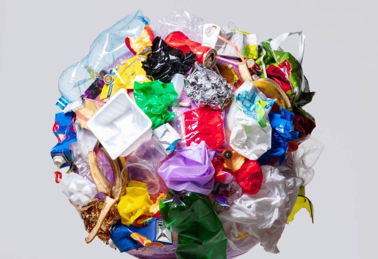 A giant wad of various metal, plastic, glass, organic, and other waste and trash floats in an empty gray field.