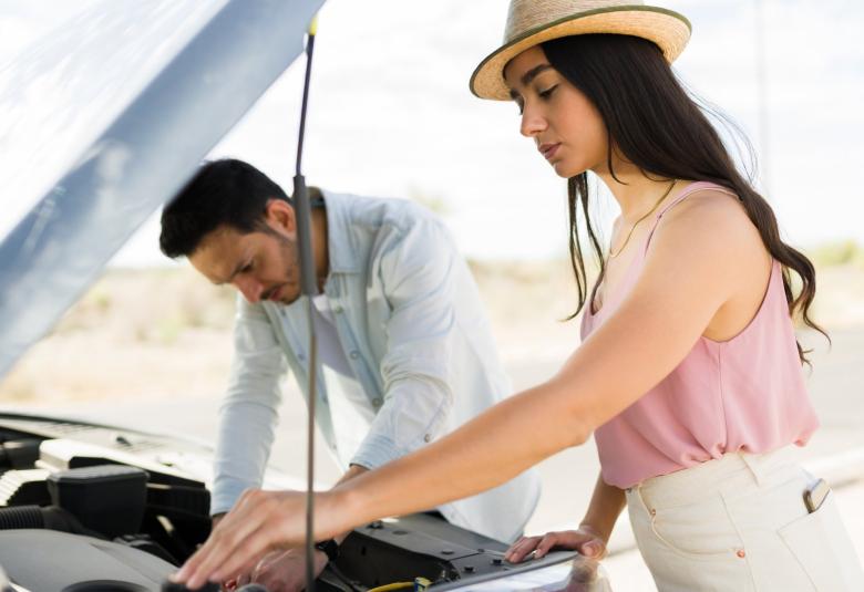 A man and a woman stand in front of a vehicle with the hood propped open. They both check a different component.