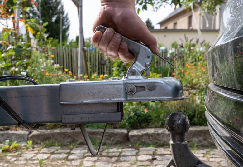 A close-up of a hand attaching a trailer to a vehicle by putting the trailer hitch lock over the towing ball.