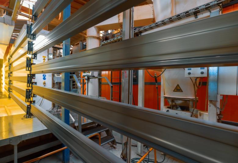 Extended molded pieces of metal being coated and cured with yellow powder coating on an assembly line.