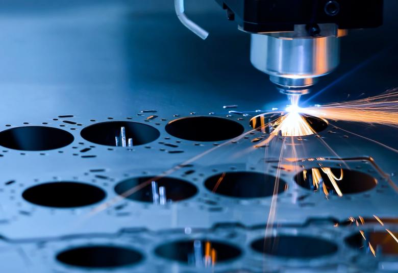 A CNC milling machine cuts a circle into a thin metal sheet, emitting orange sparks from the cutting point.