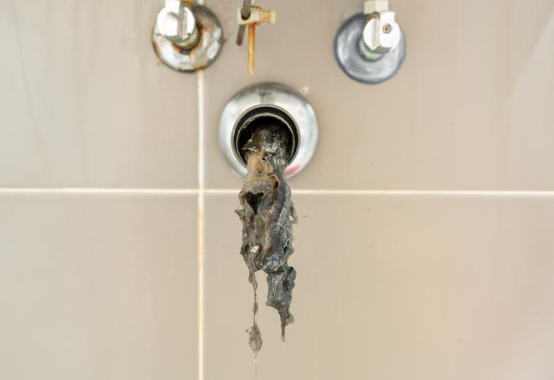 An open pipe extending from a wall with an unknown slimy substance spilling out and dangling from within.